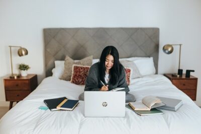 why not work from home photo of woman sitting in bed with laptop and books